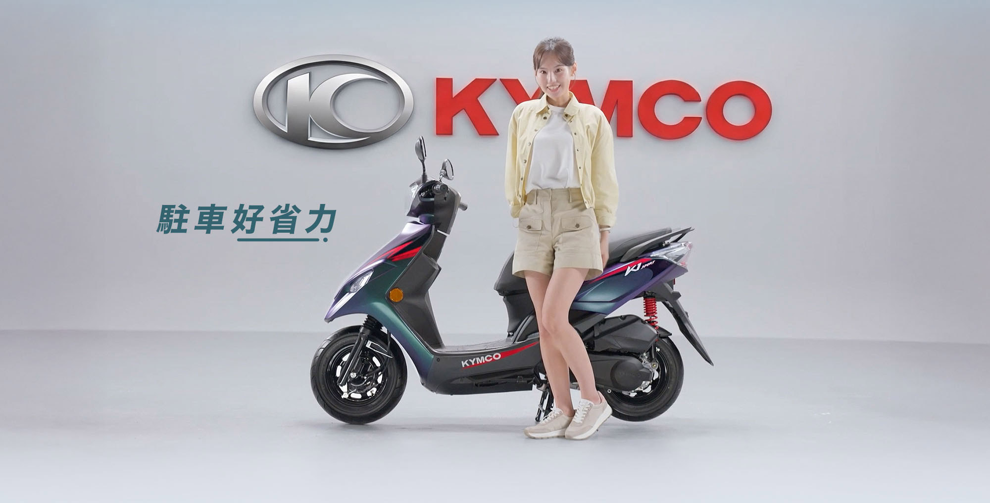 K1E 125展示女性站立於車側的駐車情境,強調日常牽車與停車操作更省力